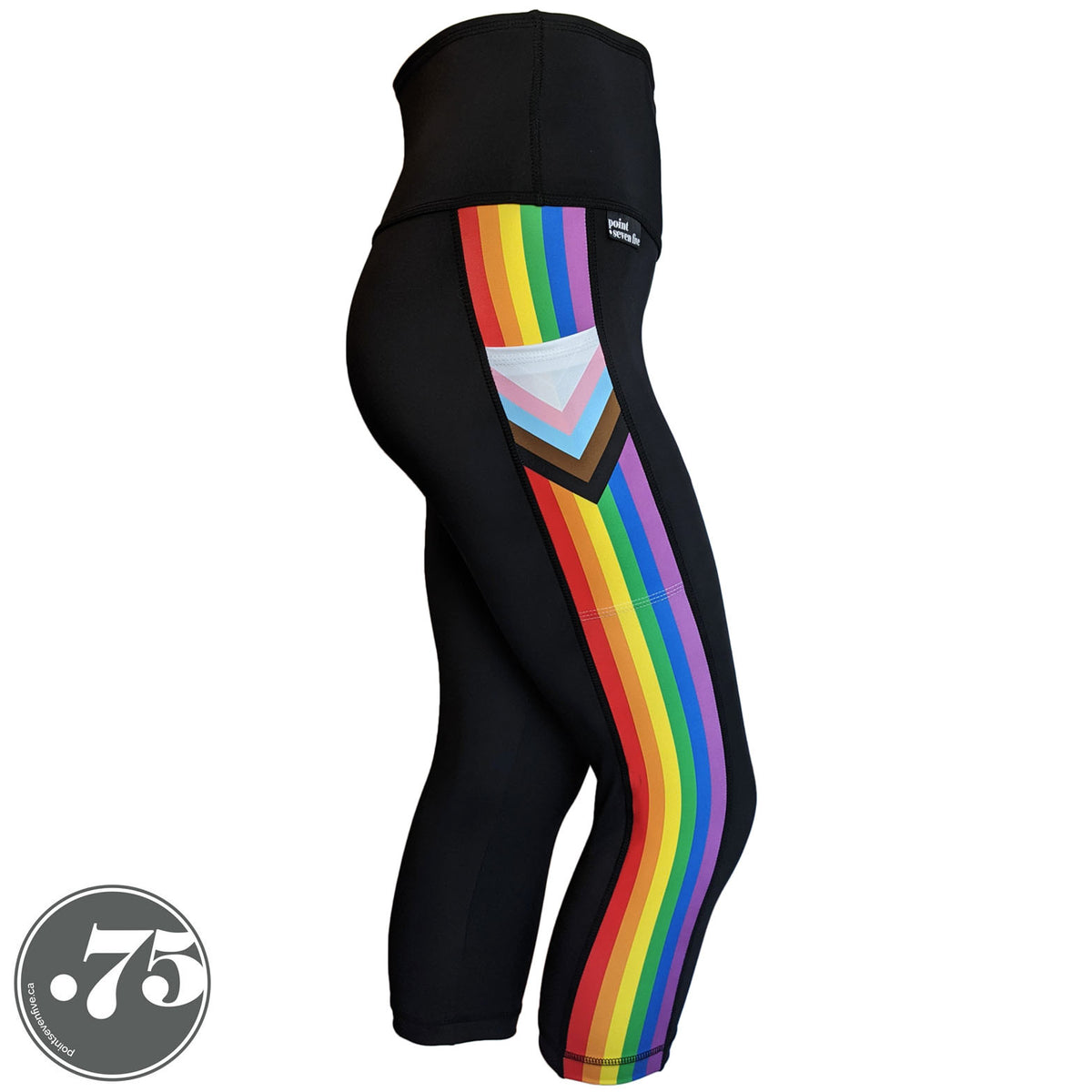 A pair of black spandex capri leggings on a mannequin, the leggings have a 3.5” wide stripe down the side that has a printed fabric with the stripes of the Progress Pride Flag vertically and the are chevrons placed at the top of the pocket. The stripes are red, orange, yellow, green, blue and purple. The chevrons are white, pink, light blue, brown and black and point down from the top of the pocket.
