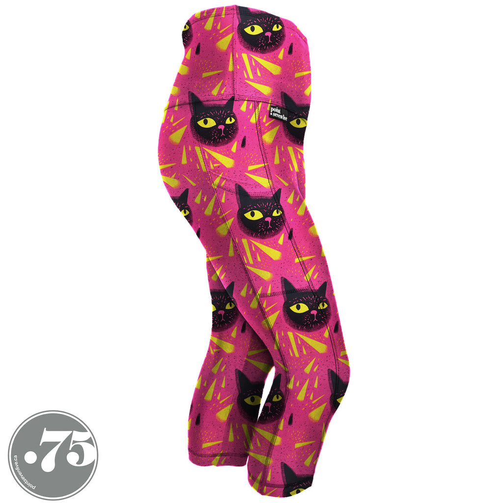High-waisted, spandex Capri Length pocket leggings. The fabric has a bright pink background with yellow triangle shapes and large hand drawn cat heads with yellow eyes.