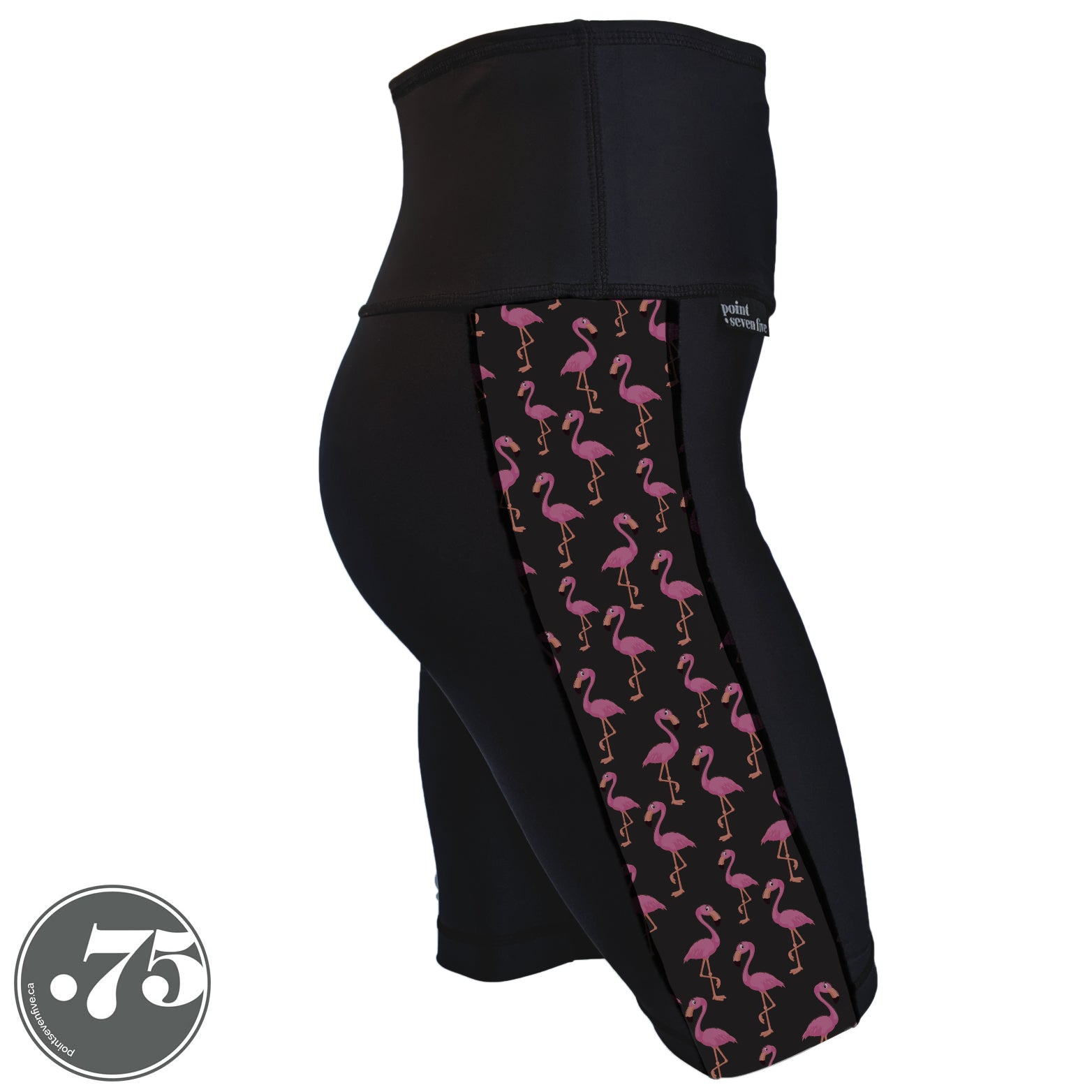 A pair of black spandex shorts against a white background. The shorts are long knee length and have a panel on the side with a pocket, the panel has fabric with a charcoal grey background with scattered cartoon pink flamingos on it.