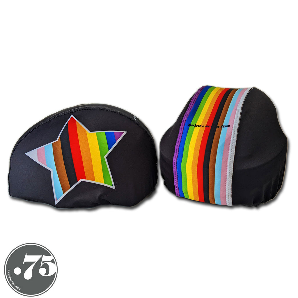 Two black helmet covers on two different helmets. The left cover has a star on it with stripes in the colours of the inclusive pride flag. The right cover has a stripe down the middle with stripes in the colours of the inclusive pride flag. 