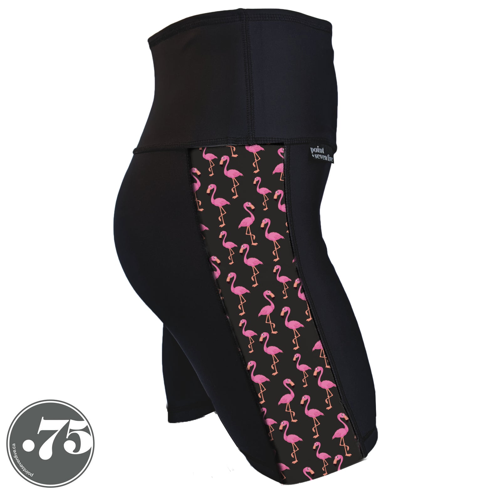 A pair of black spandex shorts against a white background. The shorts are mid thigh length with an 8" inseam and have a panel on the side with a pocket, the panel has fabric with a charcoal grey background with scattered cartoon pink flamingos on it.