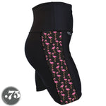 Load image into Gallery viewer, A pair of black spandex shorts against a white background. The shorts are mid thigh length with an 8&quot; inseam and have a panel on the side with a pocket, the panel has fabric with a charcoal grey background with scattered cartoon pink flamingos on it.
