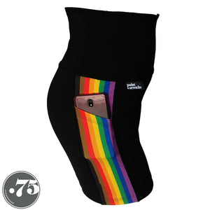 A pair of black spandex Lift length shorts on a mannequin, the leggings have a 3.5” wide stripe down the side that has a printed fabric with the stripes of the Philadelphia Pride Flag vertically, the stripes are black, brown, red, orange, yellow, green, blue & purple. There is a phone in the pocket,