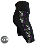 Load image into Gallery viewer, A pair of black spandex knee length shorts on a mannequin, the leggings have a 3.5” wide stripe down the side that has a printed fabric with rollerskates, helmets, stars &amp; knee pads. The graphics are in the colours of the Genderqueer Pride Flag green, purple and white. 

