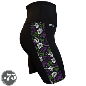 A pair of black spandex skate length shorts on a mannequin, the leggings have a 3.5” wide stripe down the side that has a printed fabric with rollerskates, helmets, stars & knee pads. The graphics are in the colours of the Genderqueer Pride Flag green, purple and white. 