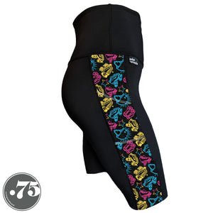 A pair of black spandex knee length shorts on a mannequin, the leggings have a 3.5” wide stripe down the side that has a printed fabric with rollerskates, helmets, stars & knee pads. The graphics are in the colours of the Pan Pride Flag pink, blue and  yellow. 