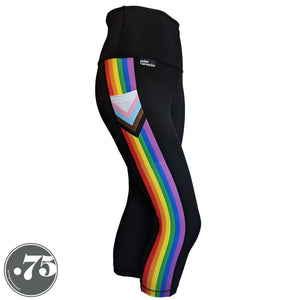A pair of black spandex capri leggings on a mannequin, the leggings have a 3.5” wide stripe down the side that has a printed fabric with the stripes of the Progress Pride Flag vertically and the are chevrons placed at the top of the pocket. The stripes are red, orange, yellow, green, blue and purple. The chevrons are white, pink, light blue, brown and black and point down from the top of the pocket. 