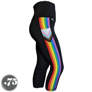 A pair of black spandex capri leggings on a mannequin, the leggings have a 3.5” wide stripe down the side that has a printed fabric with the stripes of the Progress Pride Flag vertically and the are chevrons placed at the top of the pocket. The stripes are red, orange, yellow, green, blue and purple. The chevrons are white, pink, light blue, brown and black and point down from the top of the pocket. 