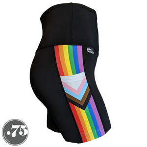 A pair of black spandex lift length shorts on a mannequin, the leggings have a 3.5” wide stripe down the side that has a printed fabric with the stripes of the Progress Pride Flag vertically and the are chevrons placed at the top of the pocket. The stripes are red, orange, yellow, green, blue and purple. The chevrons are white, pink, light blue, brown and black and point down from the top of the pocket.